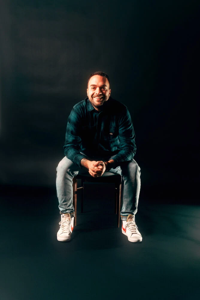 Our co-founder and managing director, seated on a chair against a black background